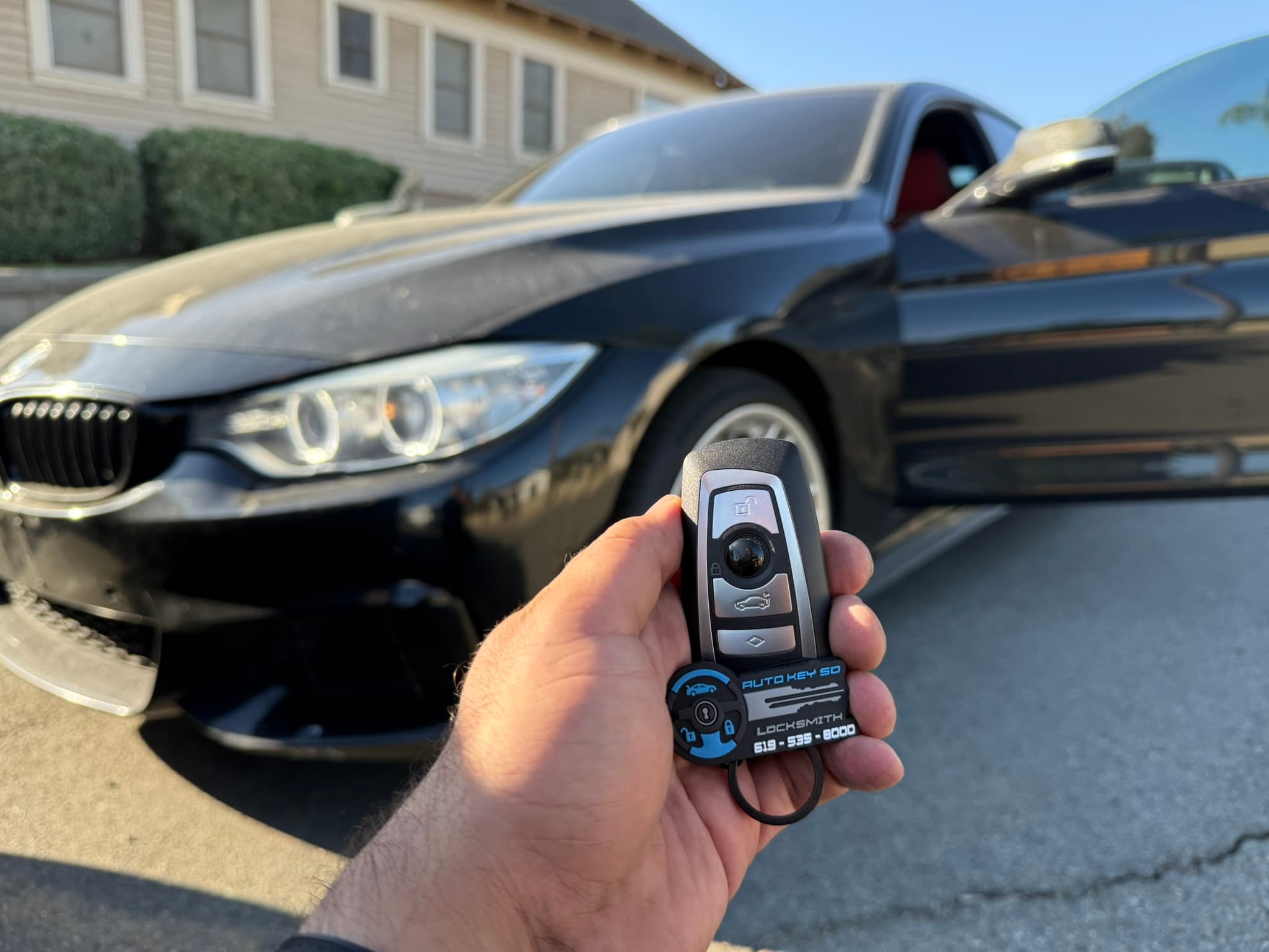 BMW remote key held beside a black BMW with its driver door open