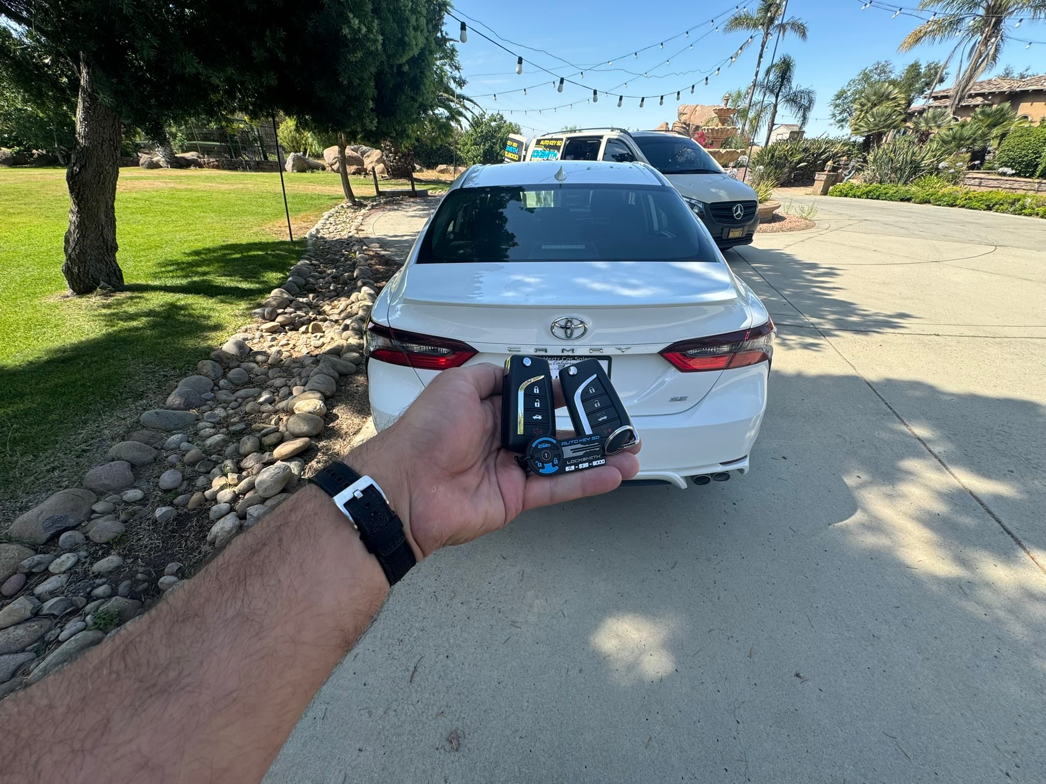 Two key fobs held behind a white Toyota Camry with the Auto Key SD van nearby